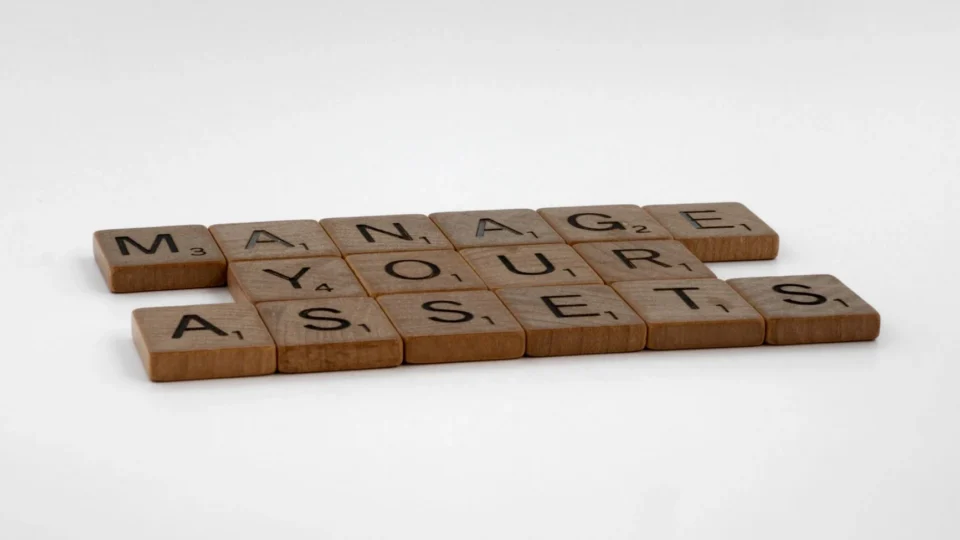 Wooden Scrabble tiles spelling 'Manage Your Assets' on a white background.