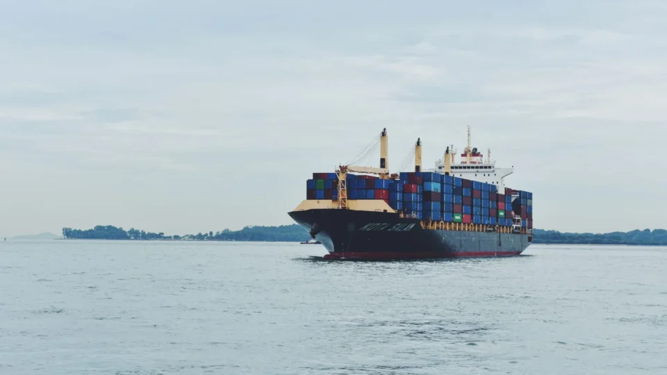 Large cargo ship transporting containers across a calm sea, symbolizing global logistics.