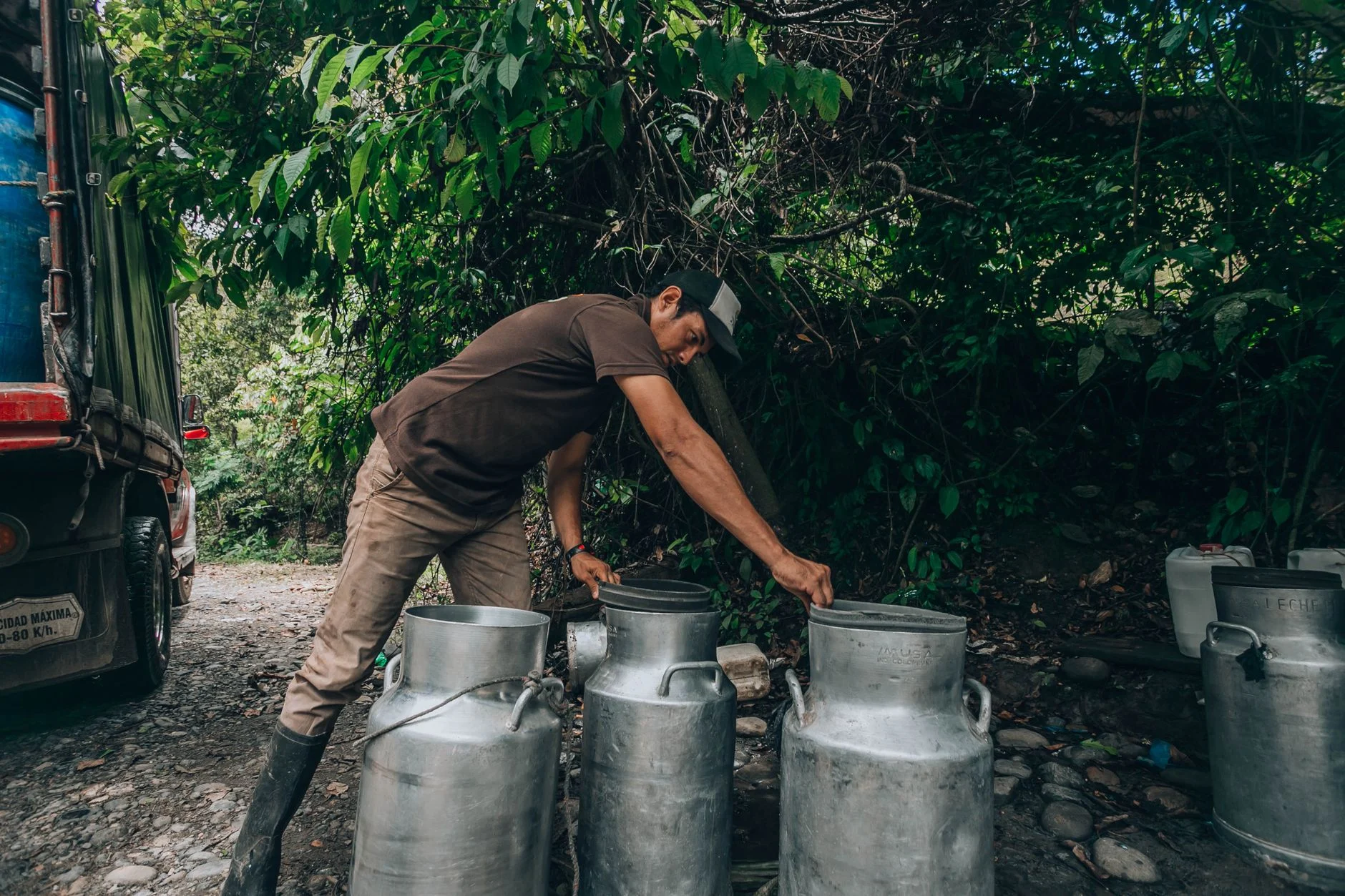 A man loading milk cans onto a truck on a forest road. Rural and outdoor scene.