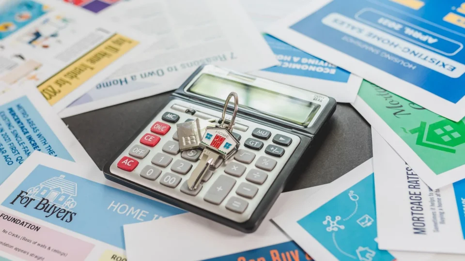 A calculator and real estate flyers depicting financial planning for home buyers.