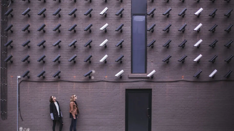 Women observing a wall covered with numerous security cameras in an urban setting, showcasing modern surveillance.