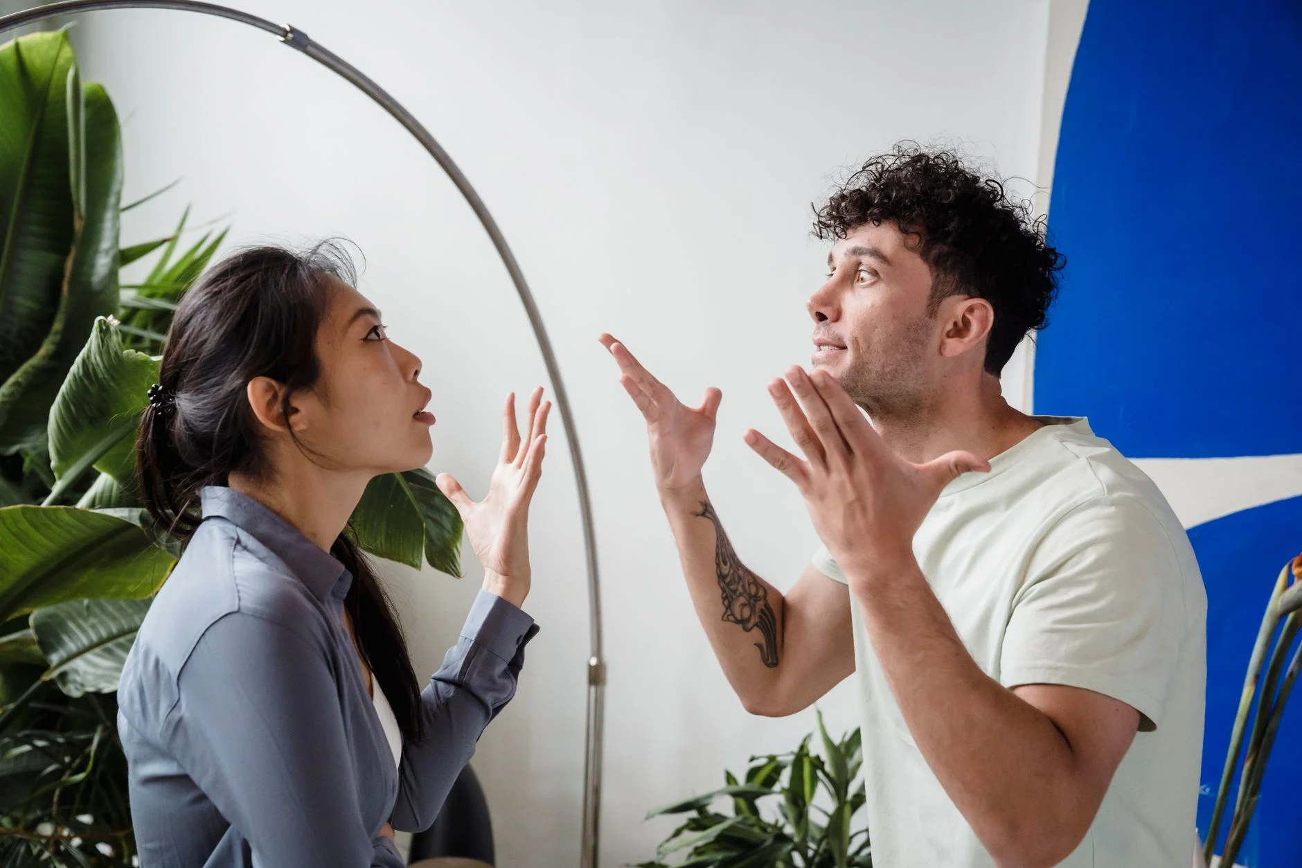 A couple argues indoors amidst greenery, showcasing emotions and interpersonal conflict.