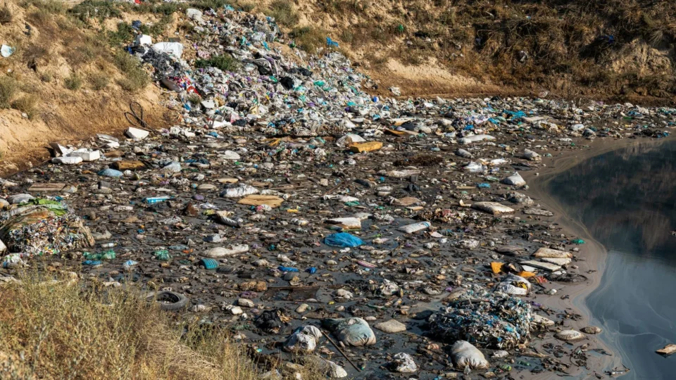 Plastic waste and debris polluting a riverbank, highlighting environmental challenges.