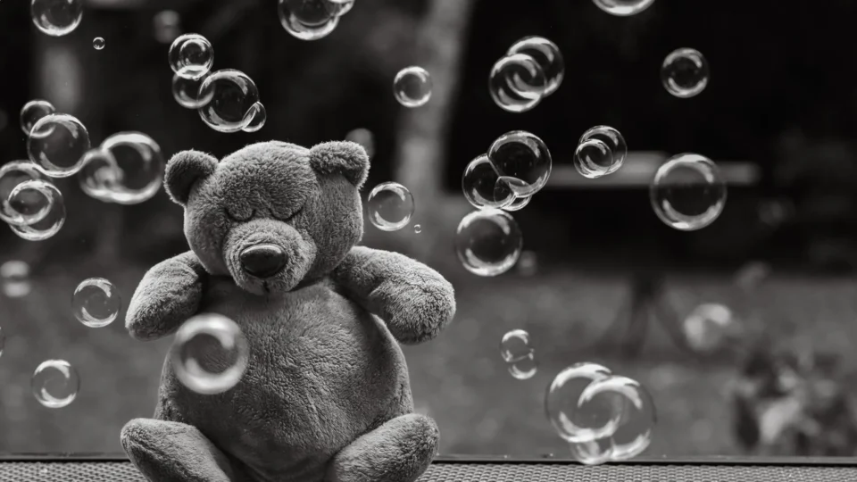 A soft teddy bear surrounded by bubbles in a serene outdoor setting, captured in black and white.