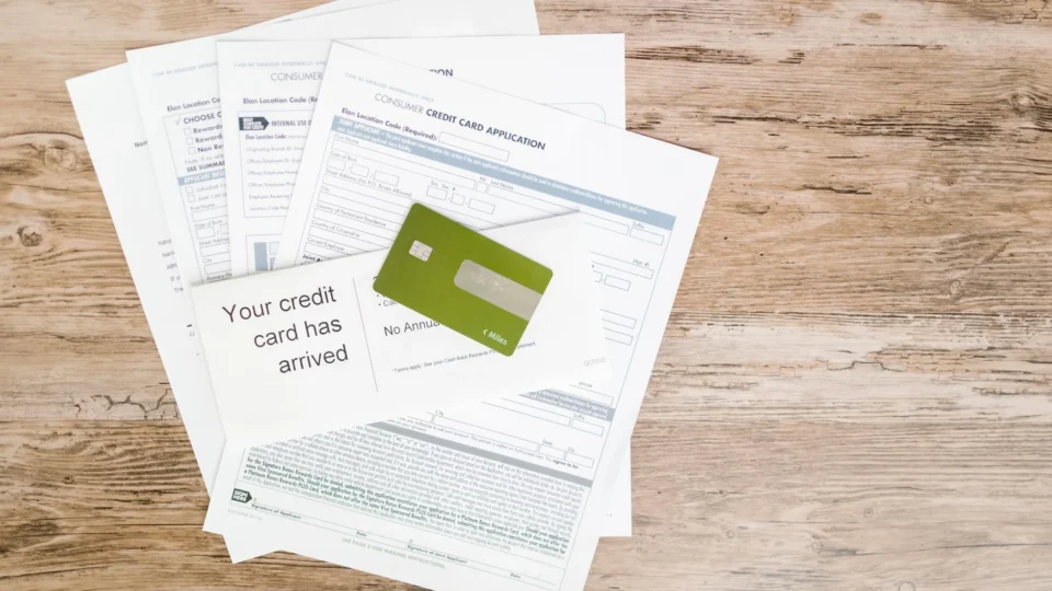 Top view of credit card and application documents on wooden surface.