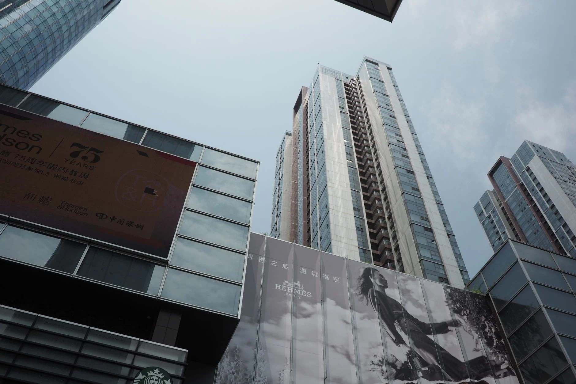 Skyscrapers with commercial billboards under a cloudy sky, depicting a modern urban scene.