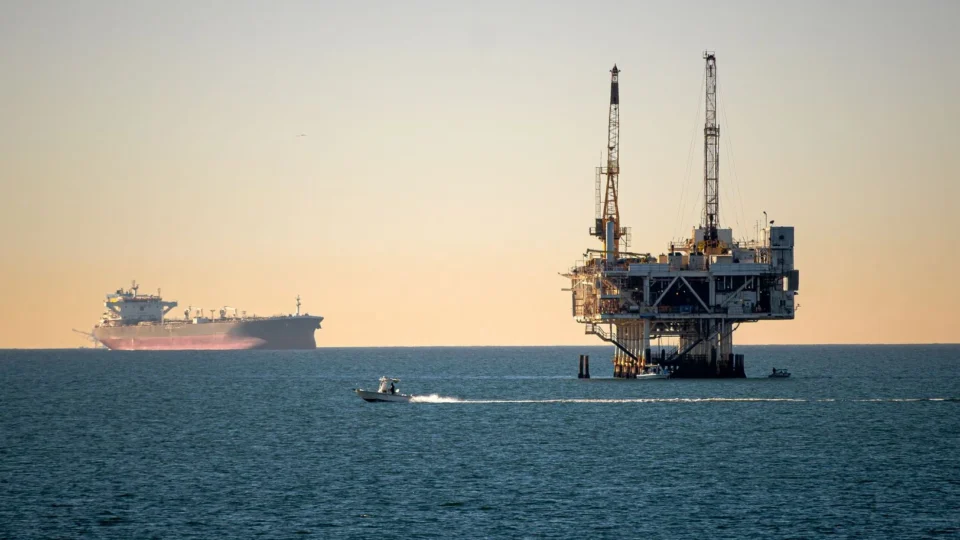 Offshore oil platform with container ship in tranquil sea during daytime.
