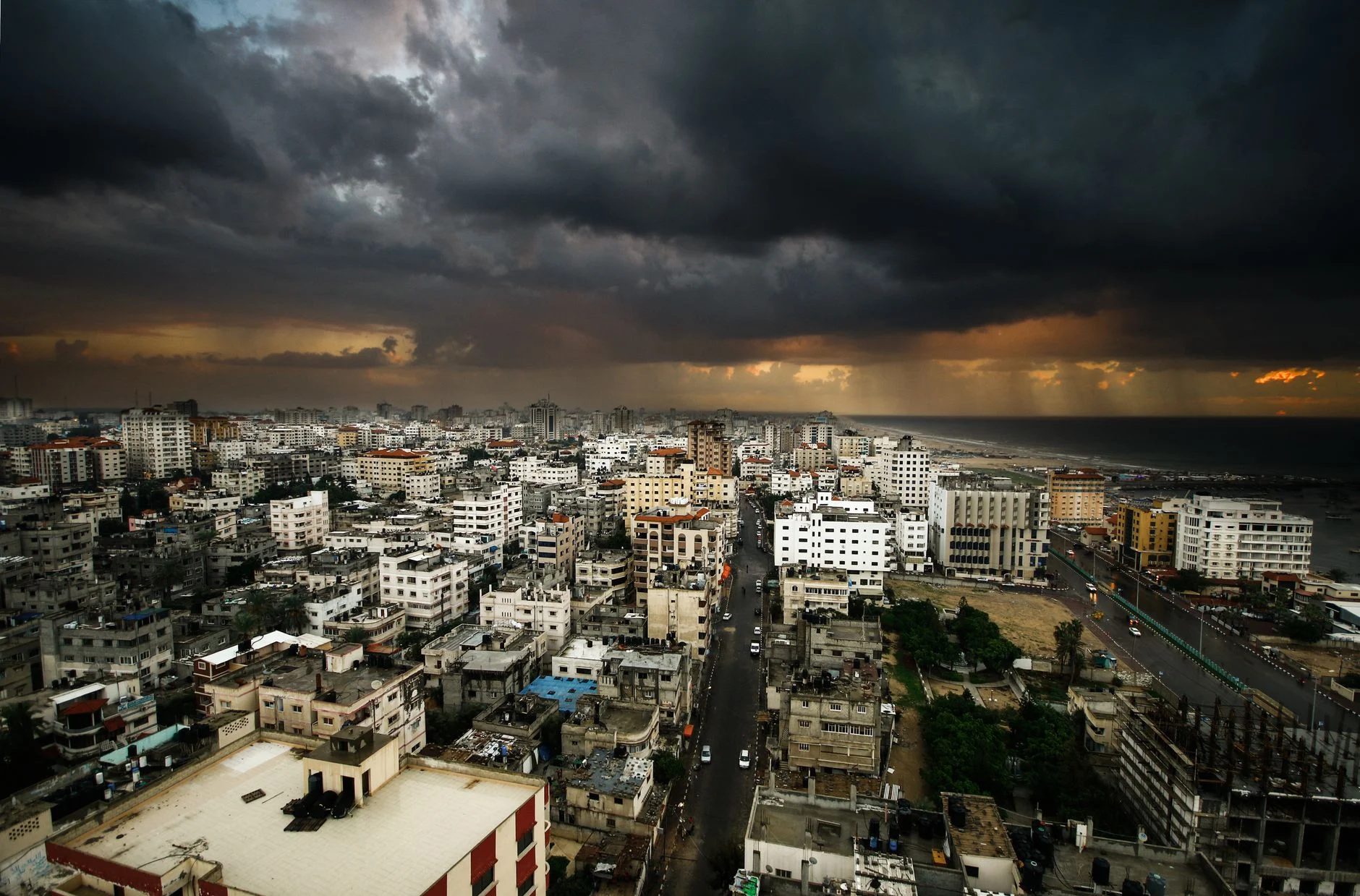 Moody city view of Gaza under dark clouds with rain on the horizon.