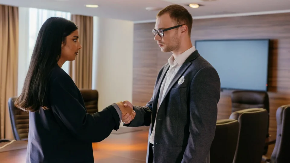 Two professionals shaking hands in a modern conference room, symbolizing successful business agreement.