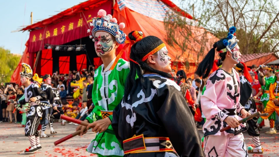 Colorful traditional Chinese opera performers in ornate costumes entertaining an outdoor audience.