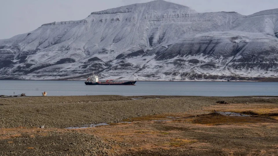 Cargo ship sails past snow-dusted mountains in Arctic scenery, capturing tranquil wilderness.