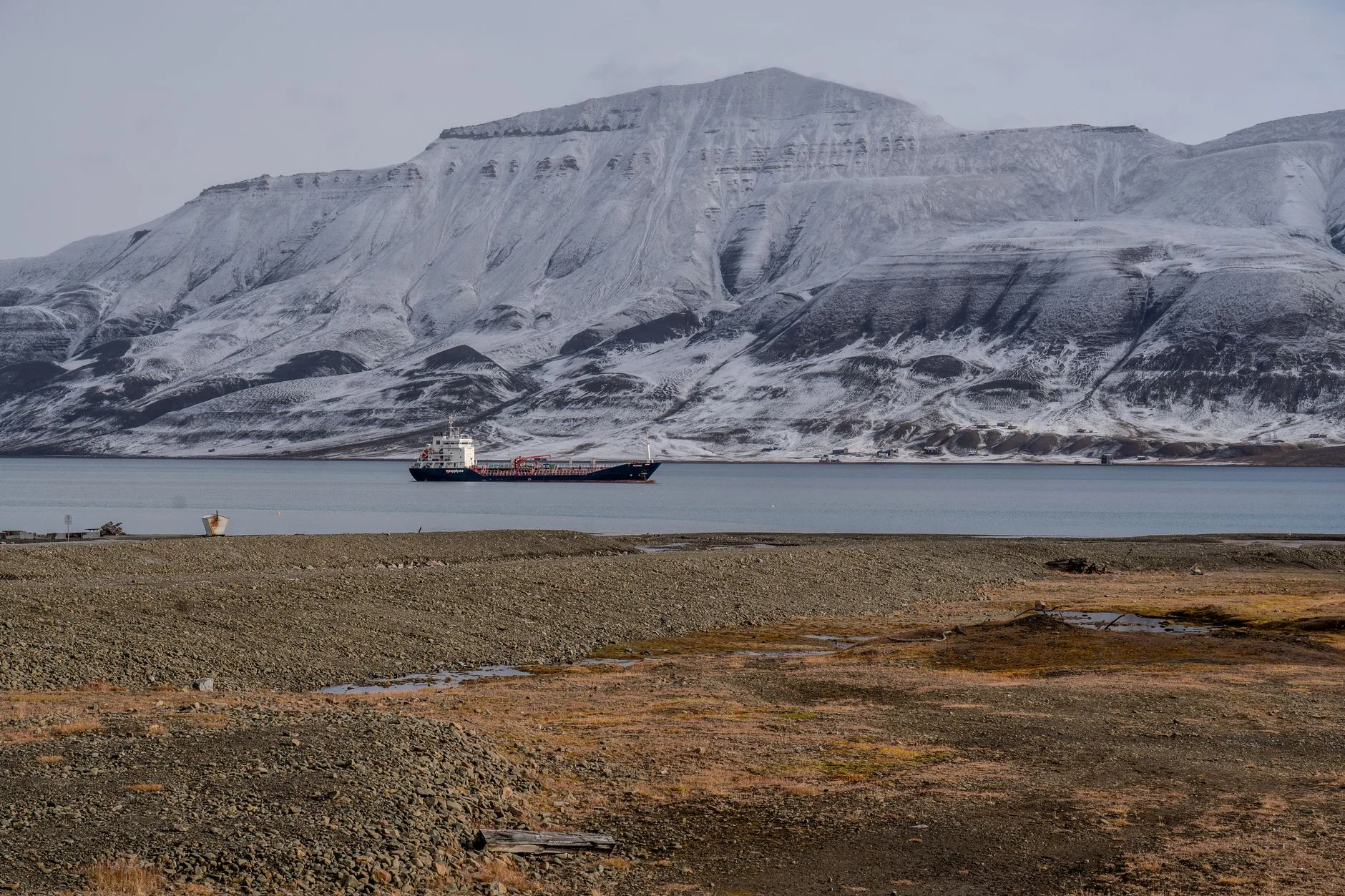 Cargo ship sails past snow-dusted mountains in Arctic scenery, capturing tranquil wilderness.
