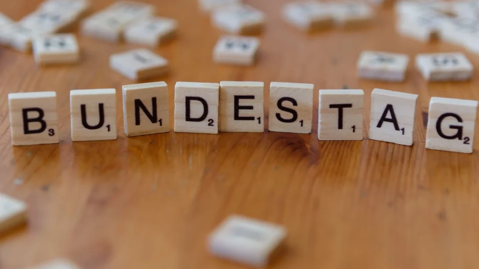 Wooden Scrabble tiles spelling 'Bundestag' on a rustic table, symbolizing German politics.