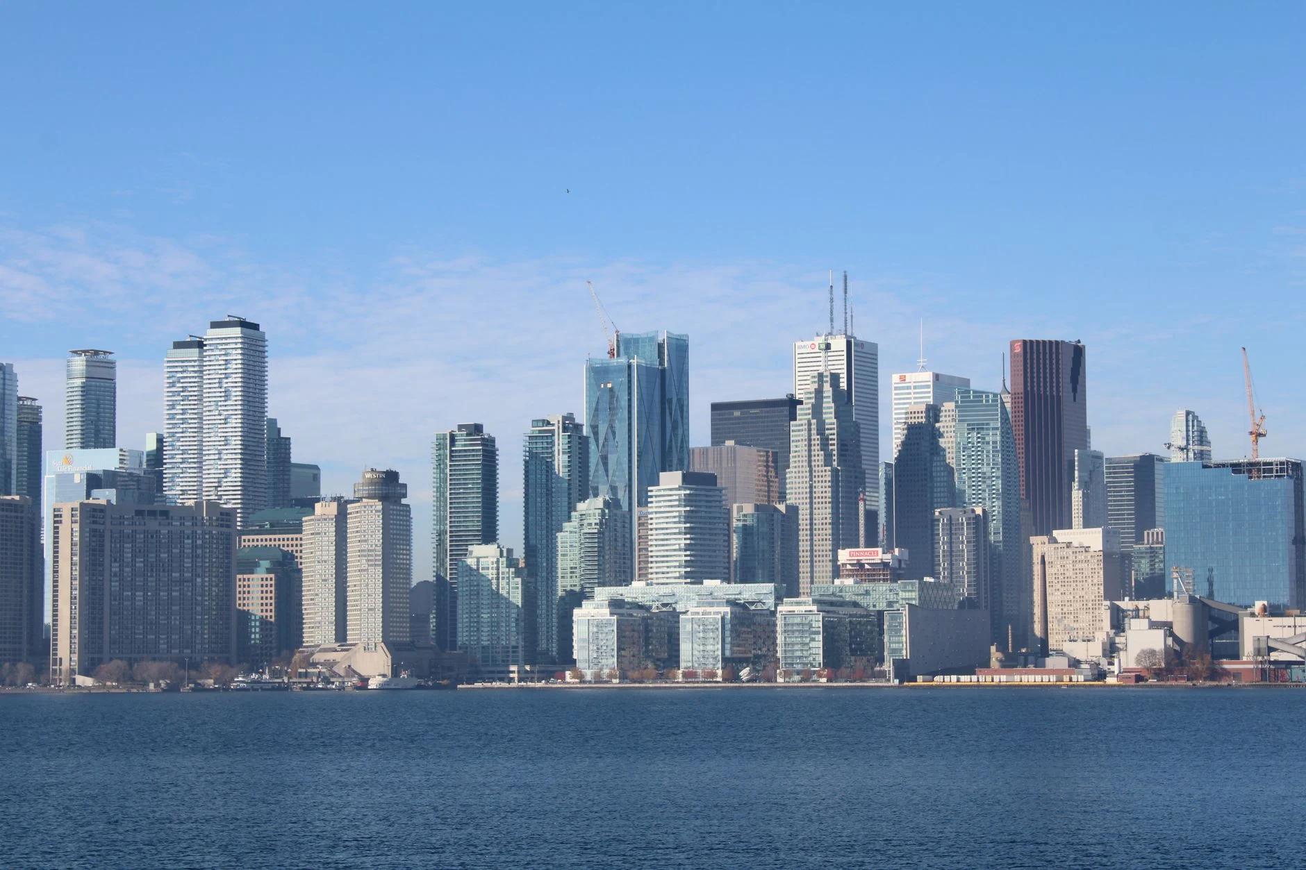 Beautiful cityscape of Toronto with modern skyscrapers reflecting in the water under a clear blue sky.
