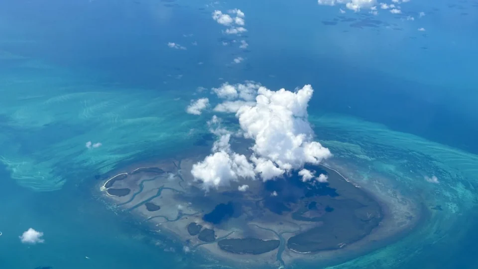 Stunning aerial view of a secluded tropical island surrounded by turquoise waters and clouds.