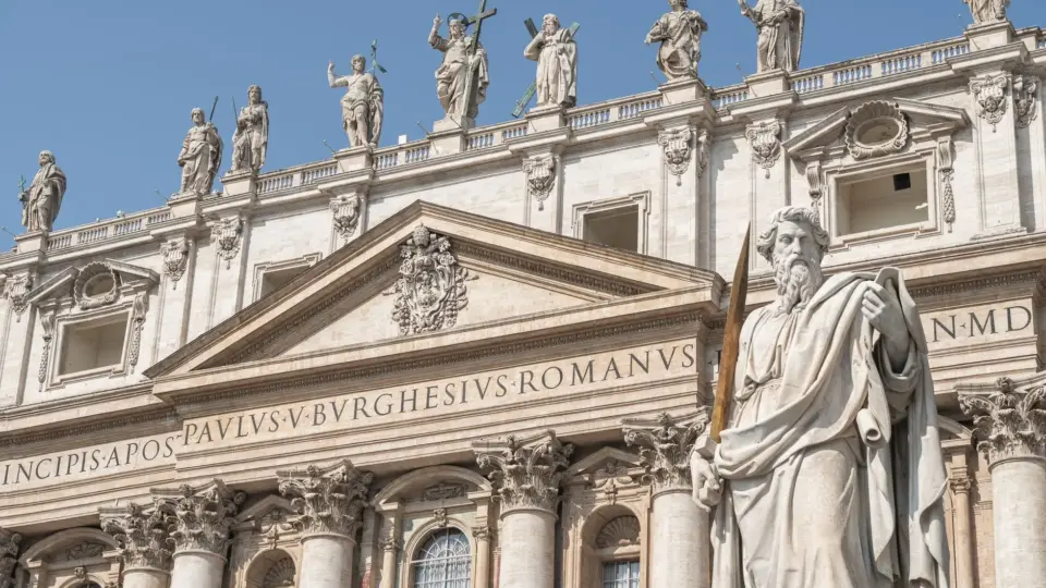 Statues of apostles adorn the facade of St. Peter's Basilica in Vatican City under a clear blue sky.
