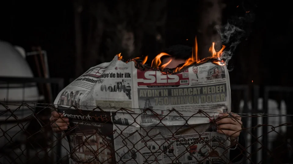 Person holding a burning newspaper outdoors, representing chaos or protest.