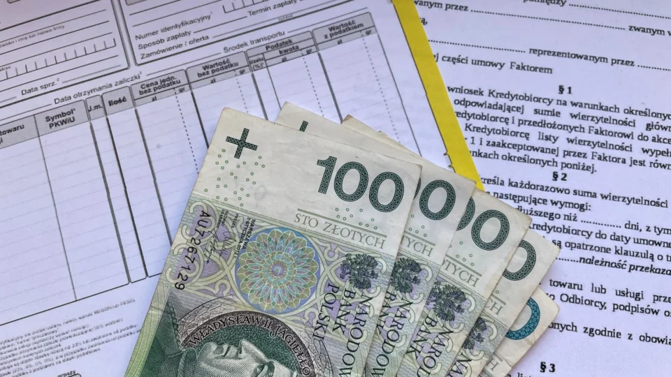 Polish 100 Zloty banknotes on VAT invoice and factoring agreement forms.