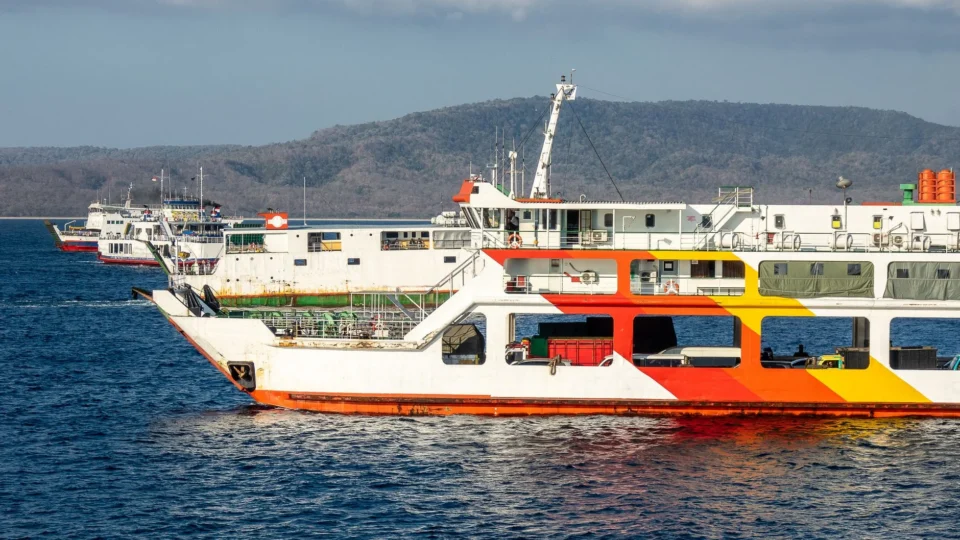 Vibrant ferries docked at a scenic harbor with mountains in the background, capturing coastal Indonesia's essence.