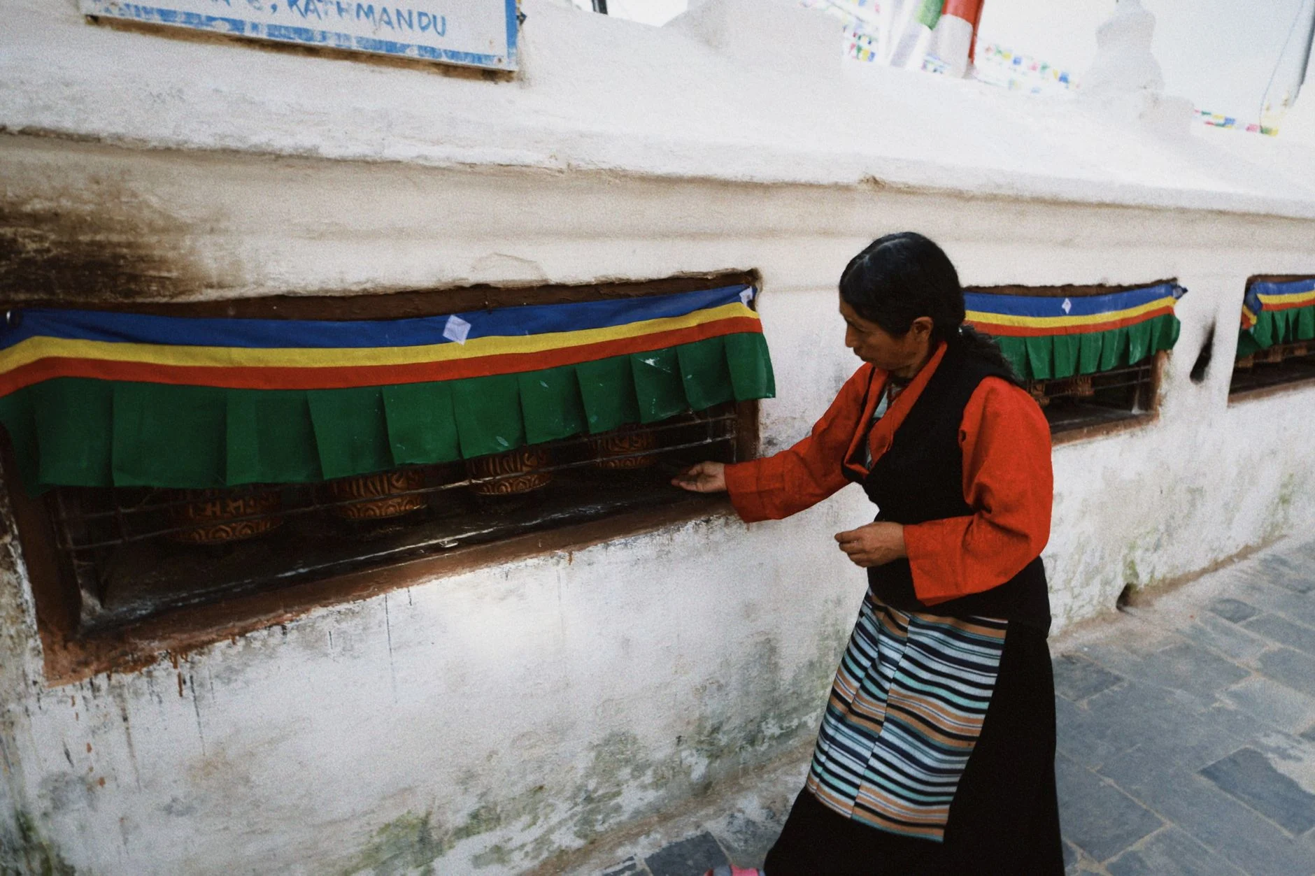 A woman in traditional attire spins prayer wheels in Kathmandu, Nepal, at a Buddhist site.
