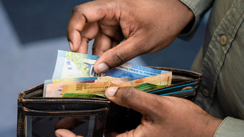 A person counting South African Rand from a wallet, symbolizing personal finance and wealth management.