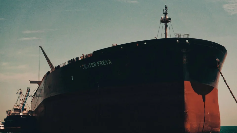 A massive cargo ship named Hunter Freya anchored at a bustling sea port under a clear sky.