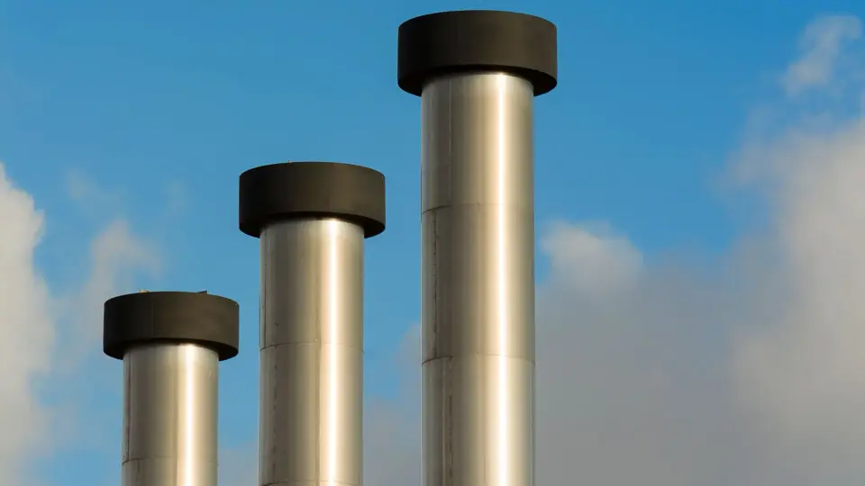 Three metallic chimneys reaching into a clear blue sky, exemplifying industrial architecture.