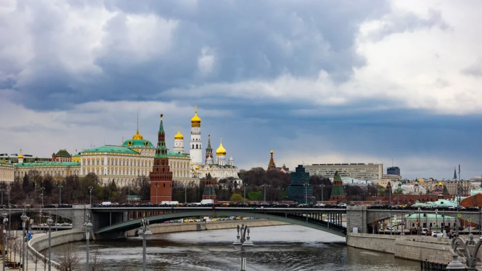 A picturesque view of the Moscow Kremlin with a bridge over the Moskva River under a dramatic sky.