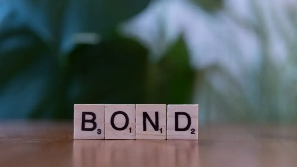 Scrabble tiles spelling 'Bond' on a wooden table with a blurred green background.