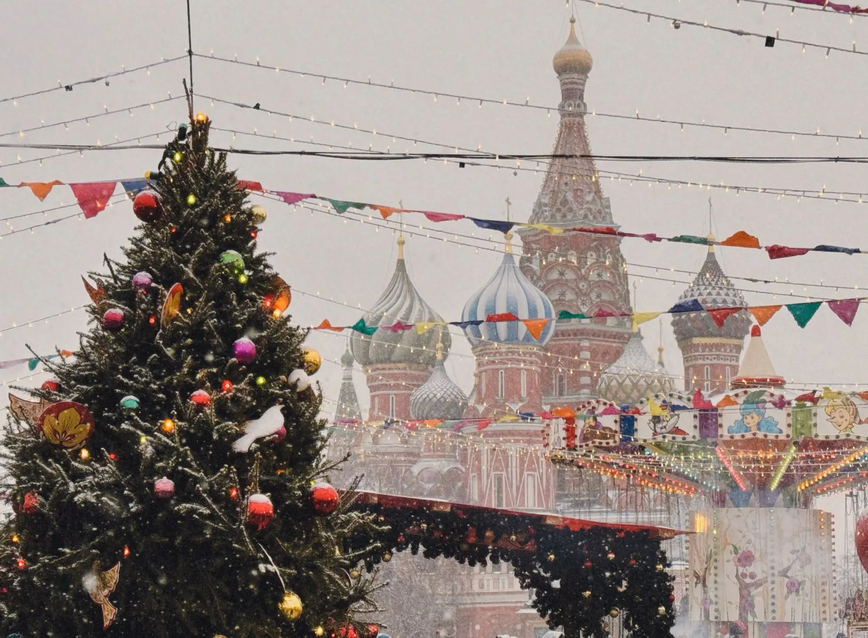 A snowy festive scene with a Christmas tree and St. Basil's Cathedral in Moscow, Russia.
