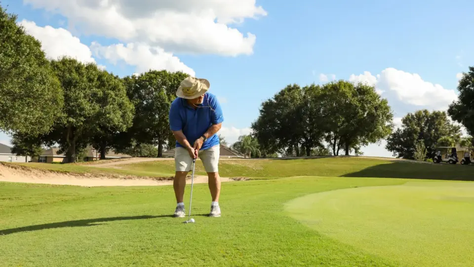 Adult male golfer putting on a sunny day at a Florida golf course with lush green landscape.